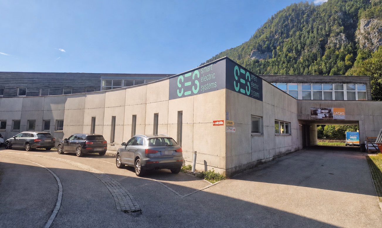 Außenansicht des Firmengebäudes von Smart Electric Systems GmbH in 4820 Bad Ischl mit Parkplatz vor dem Eingang und Bergpanorama im Hintergrund.