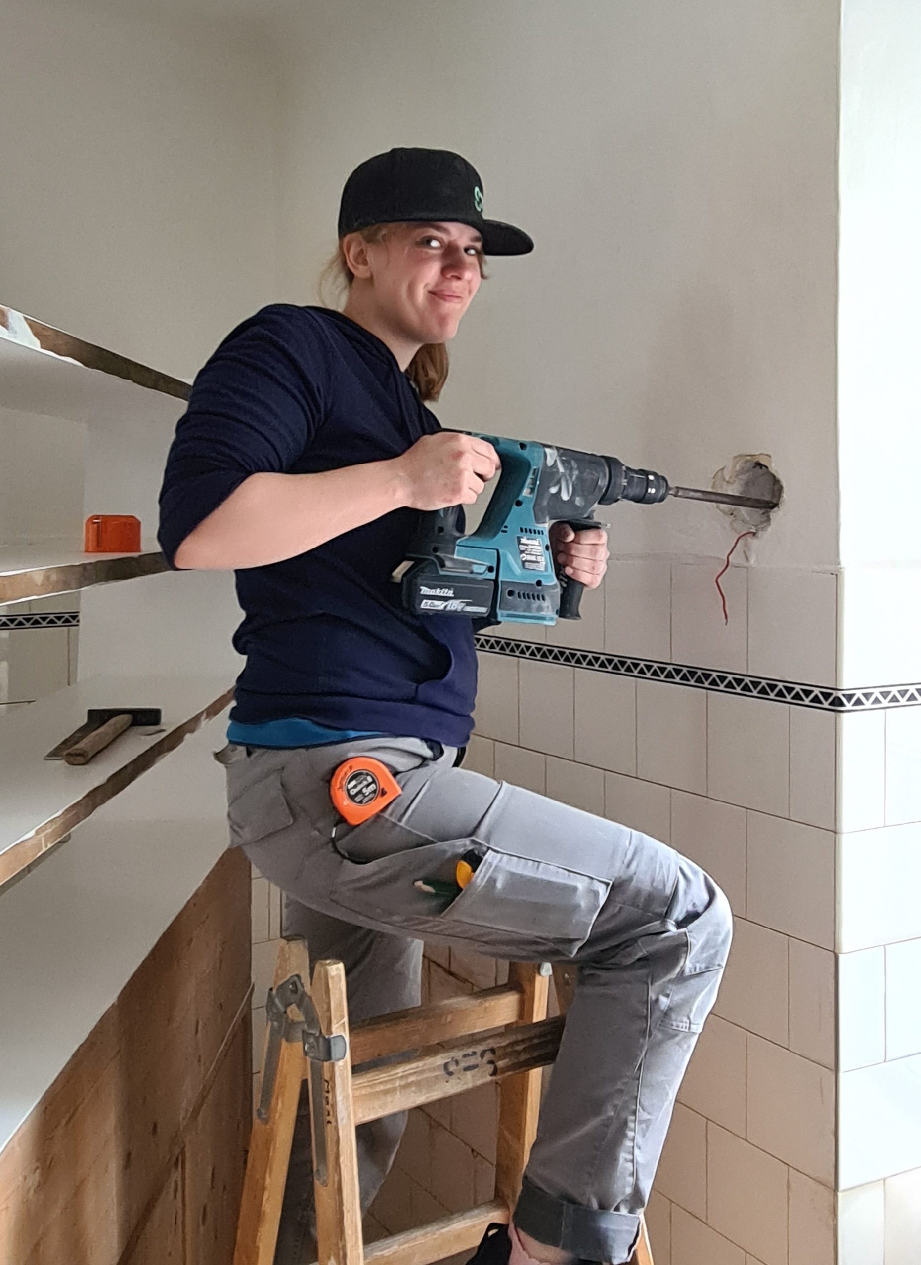 SES-Monteurin auf einer Leiter setzt mit einem Akku-Bohrhammer eine Wanddurchführung für die Elektroinstallation.
