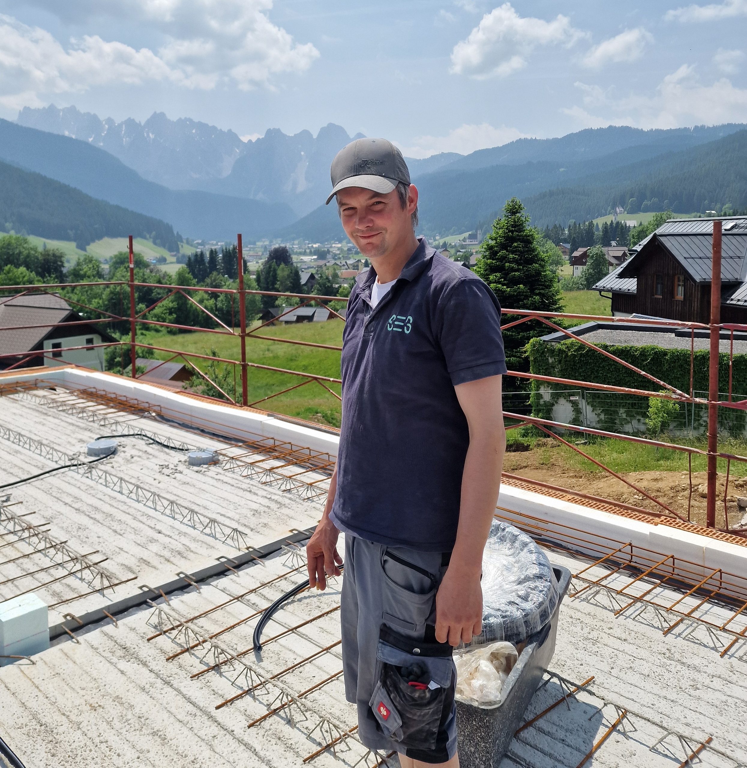 SES-Mitarbeiter im Poloshirt auf einer Neubau-Baustelle mit Blick auf die Berge des Salzkammerguts.