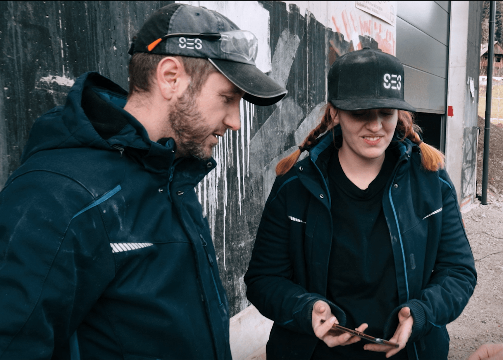 Zwei Mitarbeitende von Smart Electric Systems in Arbeitsjacken und SES-Caps besprechen einen Bauabschnitt vor Ort.